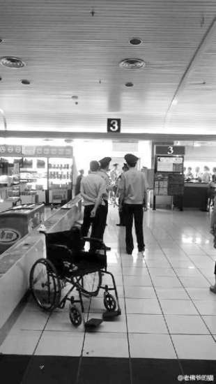 图为：机场内，几个保安和游客围在服务台前，身后有一辆空轮椅。