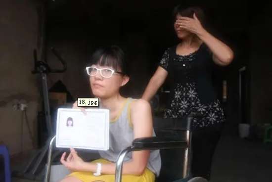 图为：刘婉玲坐在轮椅上，手持高中毕业证。
