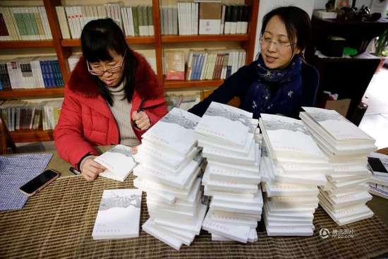 图为：余秀华面前几摞码的高高的诗集等着她签名。