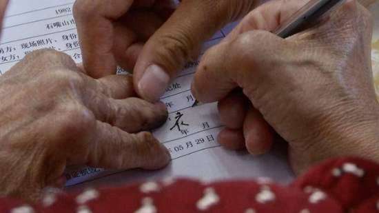 图为：患风湿手指变形且视力障碍的老年女性在离婚协议上签下自己的名字