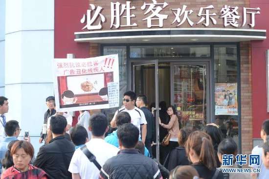 2青岛两位视障人和一名志愿者在青岛台东一路一家必胜客餐厅前进行行为艺术.jpg 图为:青岛两位视障人和一名志愿者在青岛台东一路一家必胜客餐厅前进行行为艺术,两位视障人手持的牌子上写着,“强烈抗议必胜客广告丑化残疾人”,其胸前的牌子上还印有“我不是瞎球”。