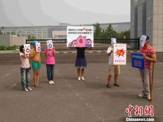 DAY13.jpg 图为:河南中医学院门前,参与活动的市民都戴着面具,其中一名扮演残障考生的市民举着高考高分成绩单,站在另一名市民扮演的河南中医学院人员前面,这位学院人员的脸扭向了一边,斜视着他,神情傲慢,伸手递给他一张录取通知书,上面写着“破格录取”,而旁边的小伙伴们看到“高分”考生竟被“破格录取”,都惊呆了。