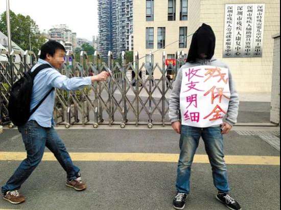 图为：深圳市残疾人综合服务中心门前上演。一名志愿者身上写着“残保金收支明细”的字样，头部被一块黑布完全罩住，残障人士马先生一剑挑去黑布。