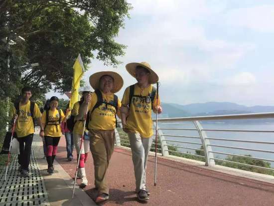 图为：第一届视障乐行徒步，一行人戴着草帽、打着旗帜，走在海边栈道上。